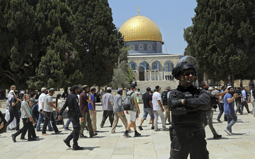 An Israeli police officer stands guard as a Jewish group walks near the Dome of the Rock Mosque atop the Temple Mount on Tisha B'Av (the ninth of Av), a day of fasting commemorating the destruction of the ancient Temples, in the Old City of Jerusalem, Sunday, July 18, 2021. (AP Photo/Mahmoud Illean)