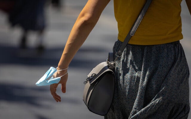 A woman holds a face mask on her wrist in Jerusalem on June 27, 2021. (Olivier Fitoussi/Flash90) A woman holds a face mask on her wrist in Jerusalem on June 27, 2021. (Olivier Fitoussi/Flash90)