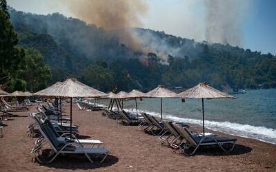 Deck chairs are seen on a beach in front of smoke and flames rising from a forest fire on August 3, 2021, in the southwestern Turkish city of Mugla, as Turkey struggles against its deadliest wildfires in decades. (Photo by Yasin AKGUL / AFP)