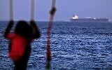 A child rides a swing as the Israeli-linked Japanese-owned tanker MT Mercer Street is seen off the port of the Gulf Emirate of Fujairah in the United Arab Emirates on  August 3, 2021 (Karim SAHIB / AFP)