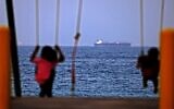 Children ride a swing as the Israeli-linked tanker MT Mercer Street is seen off the port of the Gulf Emirate of Fujairah in the United Arab Emirates, on August 3, 2021. (Karim Sahib/AFP)