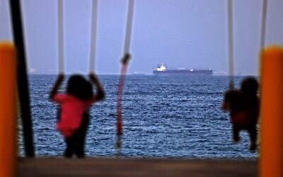 Children ride a swing as the Israeli-linked tanker MT Mercer Street is seen off the port of the Gulf Emirate of Fujairah in the United Arab Emirates, on August 3, 2021. (Karim Sahib/AFP)