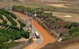 A picture taken from Lebanon's southern Marjayoun area shows an agricultural vehicle driving down a dirt road in the Israeli town of Metula along the border fence between the two countries, on August 6, 2021. (Mahmoud Zayyat/AFP)