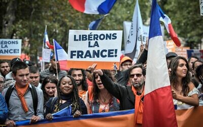Protestors hold a French flag and a sign reading 'Liberate France' during a demonstration, part of a national day of protest against the mandatory Covid-19 health pass to access most of the public space, near Ecole Militaire in Paris on August 7, 2021. (Photo by STEPHANE DE SAKUTIN / AFP)