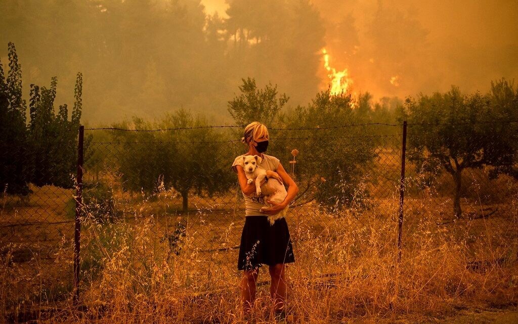 A woman holds a dog in her arms as forest fires approach the village of Pefki on Evia (Euboea) island, Greece's second largest island, on August 8, 2021 (ANGELOS TZORTZINIS / AFP) A woman holds a dog in her arms as forest fires approach the village of Pefki on Evia (Euboea) island, Greece's second largest island, on August 8, 2021 (ANGELOS TZORTZINIS / AFP)