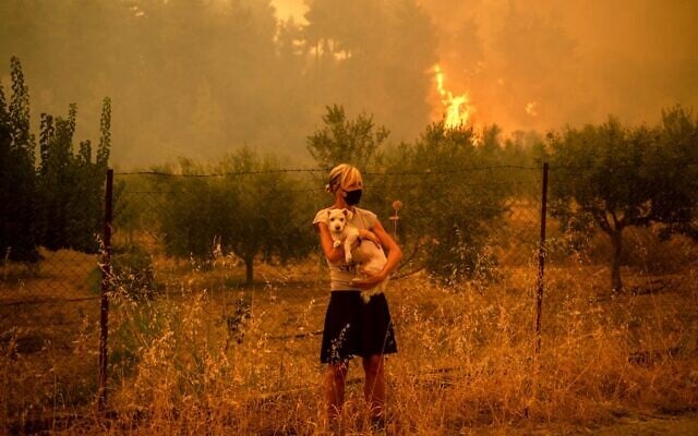 A woman holds a dog in her arms as forest fires approach the village of Pefki on Evia (Euboea) island, Greece's second largest island, on August 8, 2021 (ANGELOS TZORTZINIS / AFP)