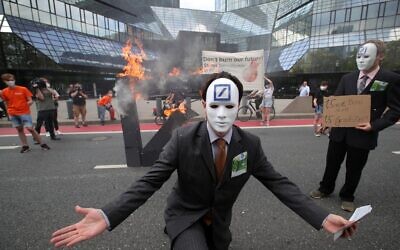 A climate activist dressed up as a banker poses in front of a burning Deutsche Bank logo in front of the bank's headquarters during a demonstration on August 13, 2021 in Frankfurt am Main, western Germany. (ARMANDO BABANI / AFP)
