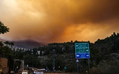 Cars drive on a road as heavy smoke and flames rise from a forest fire in the Jerusalem Hills near the Israeli village of Shoresh, on August 15, 2021. (Photo by Menahem KAHANA / AFP)