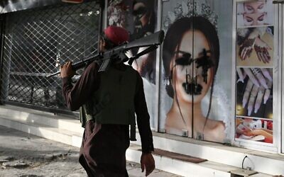A Taliban fighter walks past a beauty salon with defaced images of women in Shar-e-Naw, Kabul, August 18, 2021. (Wakil Kohsar/AFP)