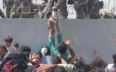 This image made available to AFP on August 20, 2021 by Omar Haidiri, shows a US Marine grabbing an infant over a fence of barbed wire during an evacuation at Hamid Karzai International Airport in Kabul on August 19, 2021.  (Courtesy of Omar Haidiri / AFP)