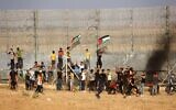 Palestinian protesters lifting national flags burn tires during a demonstration by the border fence with Israel, east of Gaza City, on August 21, 2021. (Said Khatib/AFP)