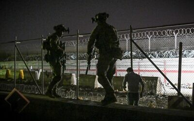 In this picture taken in the late hours on August 22, 2021, British and Canadian soldiers stand guard near a canal as Afghans wait outside the foreign military-controlled part of the airport in Kabul, hoping to flee the country following the Taliban's military takeover of Afghanistan. (Wakil Kohsar/AFP)