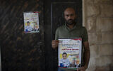 Moayyad al-Alami, father of Mohammed al-Alami, 12, carries a poster with picture and name of his son and reads "Palestinian National Liberation movement, Fatah, offers her hero martyr child," at the family house, in the West Bank village of Beit Ummar, near Hebron, August 4, 2021. (AP/Nasser Nasser)