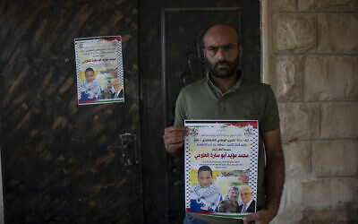 Moayyad al-Alami, father of Mohammed al-Alami, 12, carries a poster with picture and name of his son and reads "Palestinian National Liberation movement, Fatah, offers her hero martyr child," at the family house, in the West Bank village of Beit Ummar, near Hebron, August 4, 2021. (AP/Nasser Nasser)