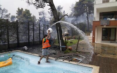 A man throws water from a swimming pool as the fire approaches his house in Ippokratios Politia village, about 35 kilometres (21 miles) north of Athens, Greece, Friday, Aug. 6, 2021.  (AP Photo/Thanassis Stavrakis)