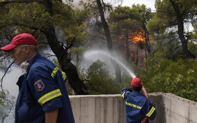 A firefighter tries to extinguish the flames outside a house in Ippokratios Politia village, about 35 kilometres (21 miles) north of Athens, Greece, Friday, Aug. 6, 2021. (AP Photo/Thanassis Stavrakis)