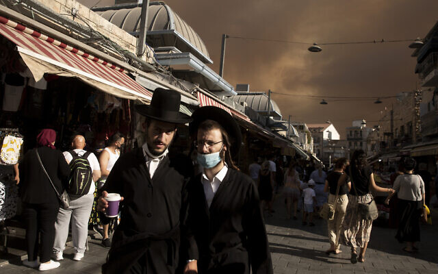 Ultra-Orthodox Jews stroll through the Machane Yehuda market under a sky darkened by nearby wildfires, in Jerusalem, August 15, 2021. (Maya Alleruzzo/AP)