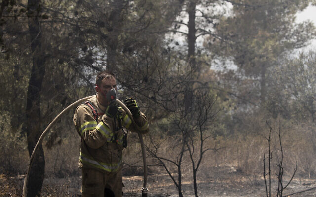 An Israeli firefighter pauses to put on a mask while battling wildfires for the second day near Shoresh, on the outskirts of Jerusalem, Aug. 16, 2021 (AP Photo/Maya Alleruzzo)