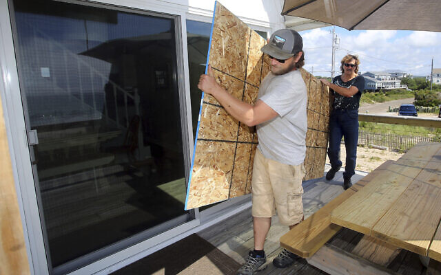 James Masog, center, and Gary Tavares, right, move particle board into place to board up the sliding glass doors of a clients house in Charlestown, R.I., ahead of Hurricane Henri, August 21, 2021. (AP Photo/Stew Milne) James Masog, center, and Gary Tavares, right, move particle board into place to board up the sliding glass doors of a clients house in Charlestown, R.I., ahead of Hurricane Henri, August 21, 2021. (AP Photo/Stew Milne)