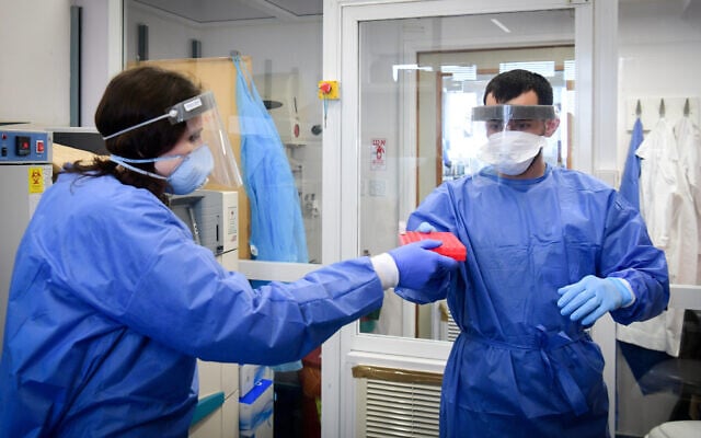 Medical staff at the Barzilai hospital, in the southern Israeli city of Ashkelon, wear protective gear, as they handle a coronavirus test sample on March 29, 2020. (Flash90) Medical staff at the Barzilai hospital, in the southern Israeli city of Ashkelon, wear protective gear, as they handle a coronavirus test sample on March 29, 2020. (Flash90)