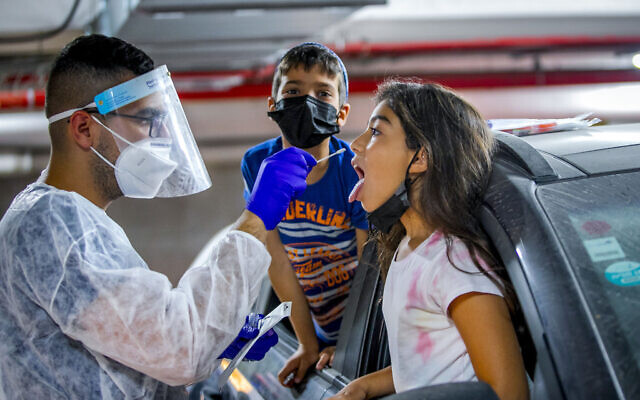Healthcare workers test a child for coronavirus at a Maccabi drive through complex in Modiin on August 15, 2021. (Yossi Aloni/Flash90) Healthcare workers test a child for coronavirus at a Maccabi drive through complex in Modiin on August 15, 2021. (Yossi Aloni/Flash90)