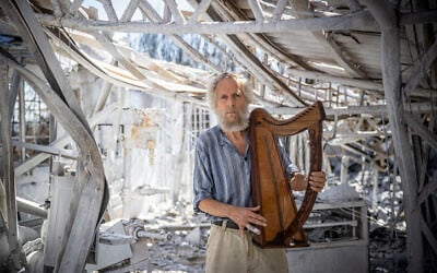 Micah Harari holds a harp at his burned harp factory in Moshav Ramat Raziel, in the Jerusalem mountains, August 18, 2021. (Yonatan Sindel/Flash90)