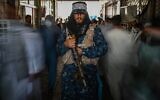 A Taliban fighter stands guard as people move past him at a market with currency exchange shops in Kabul on September 5, 2021. (Aamir Qureshi/AFP)