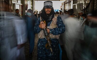 A Taliban fighter stands guard as people move past him at a market with currency exchange shops in Kabul on September 5, 2021. (Aamir Qureshi/AFP)