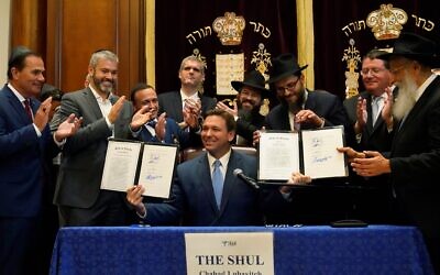 Surrounded by state legislators and Jewish leaders, Florida Gov. Ron DeSantis, center, holds up two bills that he signed on June 14, 2021, at The Shul of Bal Harbour, a Jewish community center in Surfside, Florida. (AP Photo/Wilfredo Lee)