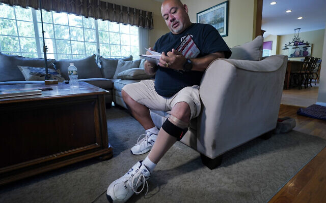 Will Jimeno, the former Port Authority police officer who was rescued from the rubble of the Sept. 11, 2001 attacks at the World Trade Center, reads from "Immigrant, American, Survivor," a children's book he wrote that draws on his experience, during an interview in his home, in Chester, N.J., Monday, Aug. 2, 2021. Injured in the attack, Jimeno wears a compression sock and leg brace band on his left leg. (AP Photo/Richard Drew)