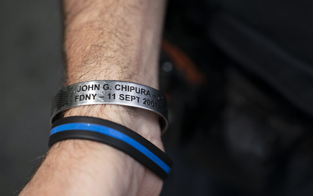 NYPD officer Michael Dougherty, a 25-year veteran, displays a bracelet bearing the name of John G. Chipura, an FDNY firefighter and former Marine who died responding to the attacks, as he stands beside the south reflecting pool of the 9/11 Memorial & Museum where names of his deceased colleagues and friends are displayed, Aug. 16, 2021, in New York (AP Photo/John Minchillo)