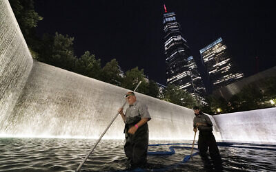 James Maroon, left, cleans the bottom of the south pool of the 9/11 Memorial with a vacuum, Aug. 4, 2021, in New York (AP Photo/Mark Lennihan)