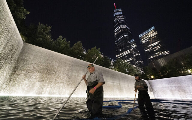 James Maroon, left, cleans the bottom of the south pool of the 9/11 Memorial with a vacuum, Aug. 4, 2021, in New York (AP Photo/Mark Lennihan)