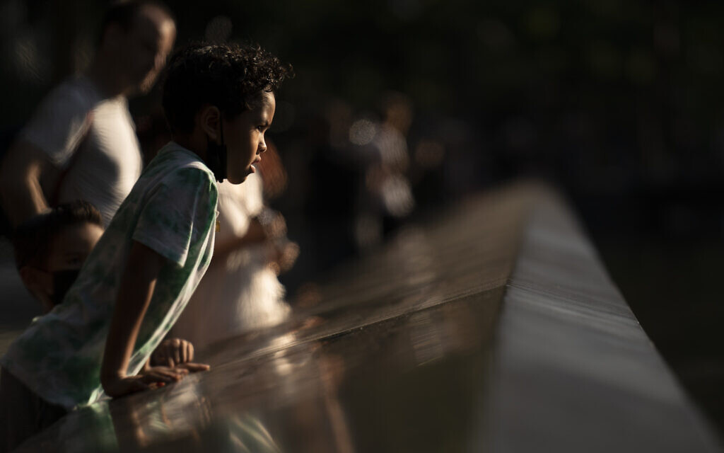 A child peers over the edge of the north pool as visitors browse the walking paths at the National September 11 Memorial & Museum,  Sept. 8, 2021, in New York. (AP Photo/John Minchillo)
