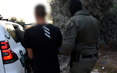 In this handout photo from September 24, 2021, a police officer walks with a suspect who was arrested in a series of raids against organized crime elements in Arab and Druze towns across northern Israel. (Israel Police)