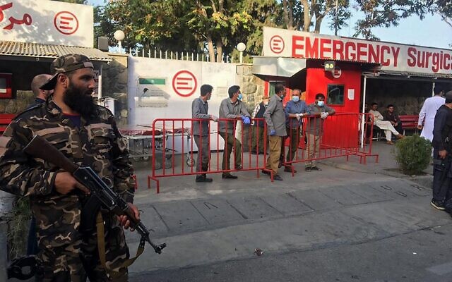 A Taliban fighter (left) stands guard as Afghan medical staff members wait at the entrance of a hospital to receive the victims of an explosion in Kabul, on October 3, 2021. (Hoshang Hashimi/AFP)