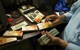 A Palestinian man counts stacks of banknotes at a currency exchange counter in the West Bank city of Ramallah on October 5, 2021. (Abbas Momani/AFP)