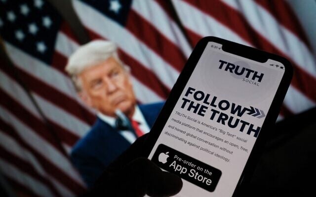 This illustration photo shows a person checking the app store on a smartphone for "Truth Social", with a photo of former US president Donald Trump on a computer screen in the background, in Los Angeles, October 20, 2021. (Chris Delmas/AFP) This illustration photo shows a person checking the app store on a smartphone for "Truth Social", with a photo of former US president Donald Trump on a computer screen in the background, in Los Angeles, October 20, 2021. (Chris Delmas/AFP)