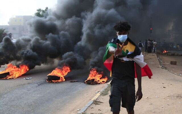 A Sudanese protester draped with the national flag flashes the victory sign next to burning tires, during a demonstration in the capital Khartoum to denounce overnight detentions by the military of members of Sudan's government, on October 25, 2021. (AFP) A Sudanese protester draped with the national flag flashes the victory sign next to burning tires, during a demonstration in the capital Khartoum to denounce overnight detentions by the military of members of Sudan's government, on October 25, 2021. (AFP)