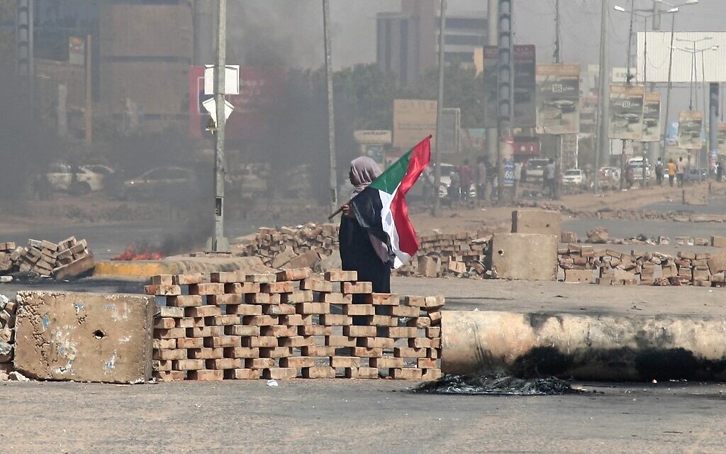 A Sudanese demonstrator carrying a national flag walks by roadblocks set up by protesters on a street in the capital Khartoum, on October 26, 2021. (AFP) A Sudanese demonstrator carrying a national flag walks by roadblocks set up by protesters on a street in the capital Khartoum, on October 26, 2021. (AFP)