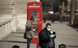 Illustrative: A man wearing a mask looks at his phone near Parliament Square, in London, March 25, 2020. (AP Photo/Matt Dunham)