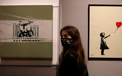 A member of staff from Bonhams auction house stands between two works by British artist Banksy: 'Girl with Balloon 2004', right, and 'Heavy Weapon' 2000, in London, Thursday, Oct. 1, 2020. (Alastair Grant/AP)