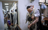 Holocaust survivor Yehoshua Datsinger places tefillin on his arm above the Auschwitz concentration camp identification number tattoo, during morning prayer at a synagogue, in Bnei Brak, Israel, September 21, 2020. (Oded Balilty/AP)