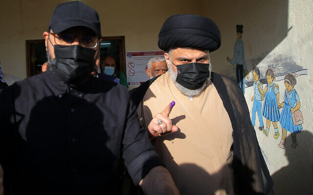 Populist Shiite cleric Muqtada al-Sadr, right, displays his ink-stained finger that shows he voted, at a polling center during the parliamentary elections in Najaf, Iraq, Sunday, Oct. 10, 2021. (AP Photo/Anmar Khalil)