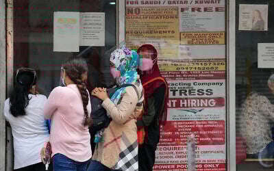 Women stand beside a sign about hiring domestic helpers for the Middle East outside an office in Manila, Philippines, October 18, 2021. (AP Photo/Aaron Favila)
