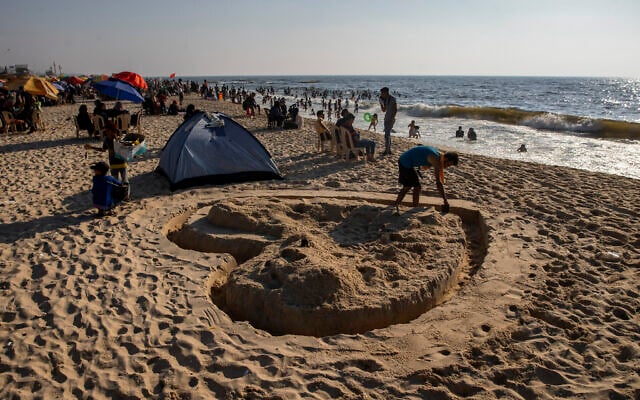 A Palestinian man works on a sand shape of heart on the beach of Gaza City,July 2, 2021. (AP Photo/Khalil Hamra)