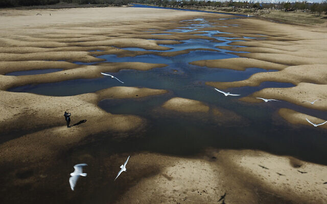 Birds fly over a man taking photos of the exposed riverbed of the Old Parana River, a tributary of the Parana River during a drought in Rosario, Argentina, July 29, 2021. (AP Photo/Victor Caivano) Birds fly over a man taking photos of the exposed riverbed of the Old Parana River, a tributary of the Parana River during a drought in Rosario, Argentina, July 29, 2021. (AP Photo/Victor Caivano)