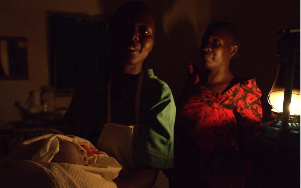 Few doctors are available in Uganda's village health clinics, many of which lack electricity. Here a midwife in the Mbale region, where the country's Jewish community lives, holds a newborn baby delivered to the light of a kerosene lantern. (Bernard Dichek)