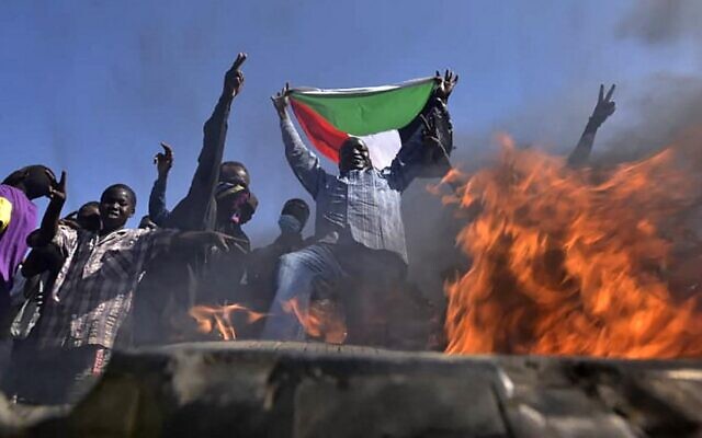 A man holds a Sudanese national flag before flames at a barricade as people protest against the military coup in Sudan, in the east of capital Khartoum on November 13, 2021. (AFP) A man holds a Sudanese national flag before flames at a barricade as people protest against the military coup in Sudan, in the east of capital Khartoum on November 13, 2021. (AFP)