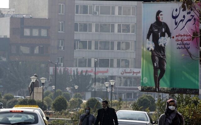 People walk past a large poster of Iranian goalkeeper Zohreh Koudaei in the capital Tehran, on November 19, 2021. (AFP) People walk past a large poster of Iranian goalkeeper Zohreh Koudaei in the capital Tehran, on November 19, 2021. (AFP)
